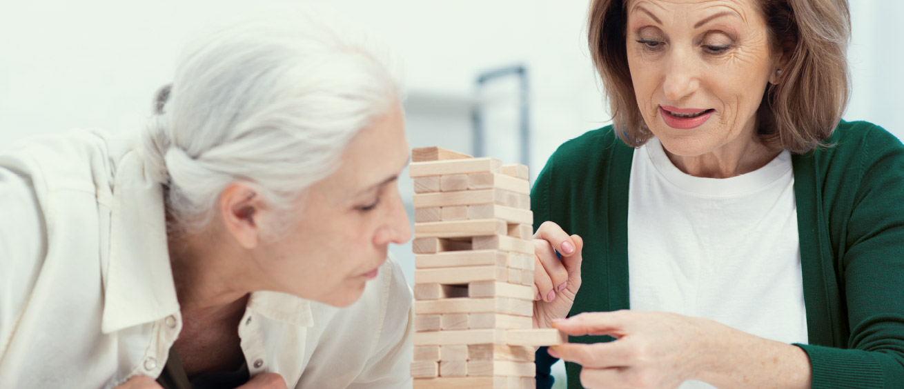 Zwei Frauen spielen an einem Tisch Türmchen bauen.