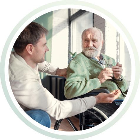 Ein junger Mann hilft einem Älteren der im Rollstuhl sitzt.